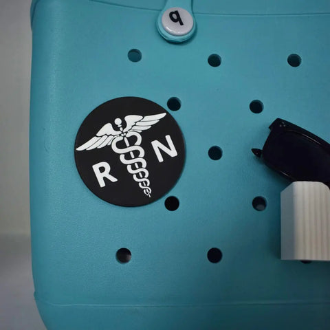The Boglets RN Nurse Charm by Chatelet Manufacturing features a black circular RN badge with caduceus, perfect for decorating Bogg Bags or Simply Southern totes—ideal as nurse gifts or stylish personalized bag charms.
