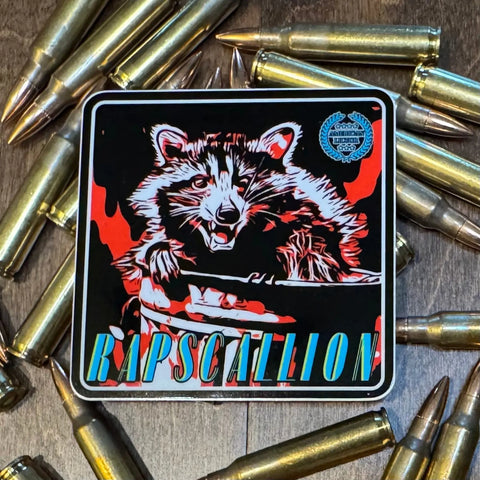 The American Lictor Sticker: Raccoon - Rapscallion features a cute raccoon in a flaming trash can, surrounded by rifle bullets, with RAPSCALLION in colorful letters at the bottom—perfect for animal lovers and sticker collectors.