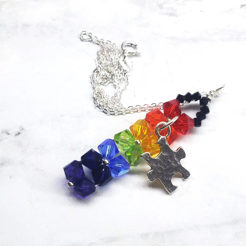 The Alexa Martha Designs Wire Woven Rainbow Autism Puzzle Piece Bar Necklace-2024 Limited Edition features faceted rainbow beads and a silver puzzle piece charm, shown on a white marble background.