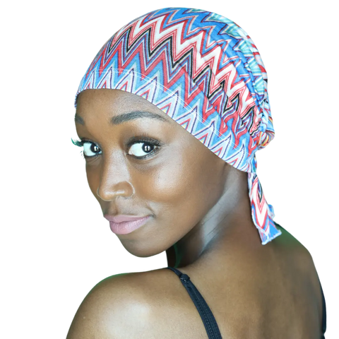 A woman with smooth brown skin smiles softly over her shoulder, wearing the colorful Louisa Chemo Beanie® by Chemo Beanies® and a black strap top against a white background.