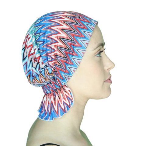 A woman in profile wears the Chemo Beanies® Louisa, a chemo beanie with bold red, blue, and white zigzag patterns on black.