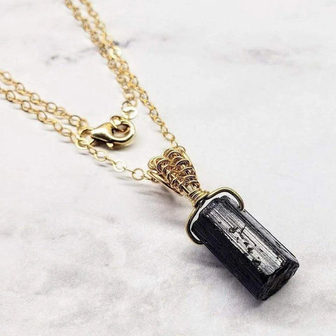 The Raw Black Tourmaline Gemstone Necklace by Alexa Martha Designs features a gold filled wire wrapped raw crystal pendant, elegantly displayed on light marble—a stunning example of handmade Montana jewelry.