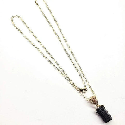 The Raw Black Tourmaline Gemstone Necklace by Alexa Martha Designs features a gold filled wire-wrapped pendant on a delicate gold chain, beautifully displayed on a white background—a stunning piece of handmade Montana jewelry.