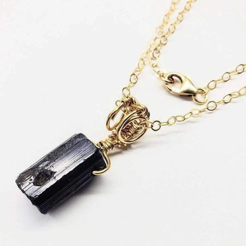 The Raw Black Tourmaline Gemstone Necklace by Alexa Martha Designs features a rough black stone pendant on a gold filled wire wrapped chain, highlighting artisan details and Montana handmade quality. Displayed on a white background.