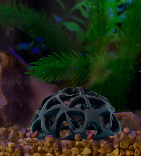 The Chatelet REEFSHAPE Dome Fish or Shrimp Aquarium Hideout by Chatelet Manufacturing rests on brown gravel among green aquatic plants, with a blurred background adding depth. Made in the USA, its perfect for aquarium decor and observation.