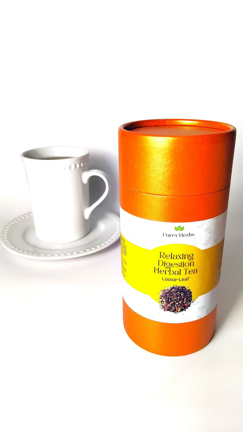 A Forev'Herbs Relaxing Digestion Herbal Tea orange canister stands by a white cup and saucer, showcasing this caffeine-free herbal tea for digestive support against a plain white background.