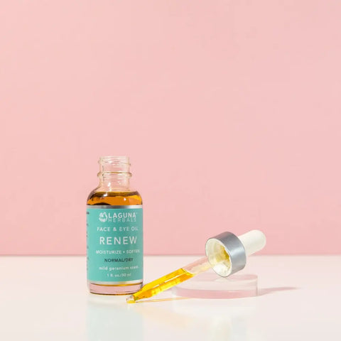 A bottle of Laguna Herbals RENEW Face Oil for normal to dry skin sits beside its dropper filled with yellow oil, all displayed against a pink background.