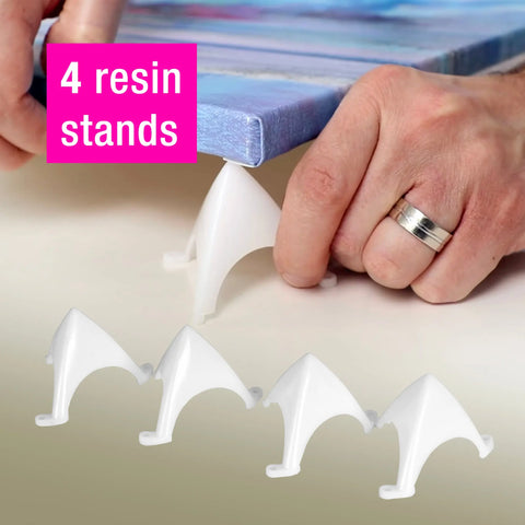 A hand places an ArtResin Accessory Kit white resin stand under a canvas corner, with four stands visible below for pro-level resin art. Pink text shows 4 resin stands. Brand: ArtResin.