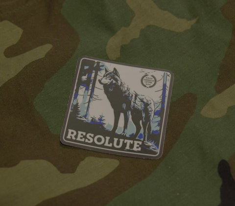 The Sticker: Wolf - Resolute by American Lictor features a wolf illustration above the word RESOLUTE, set against a camouflage background—symbolizing silent movement and coordination.