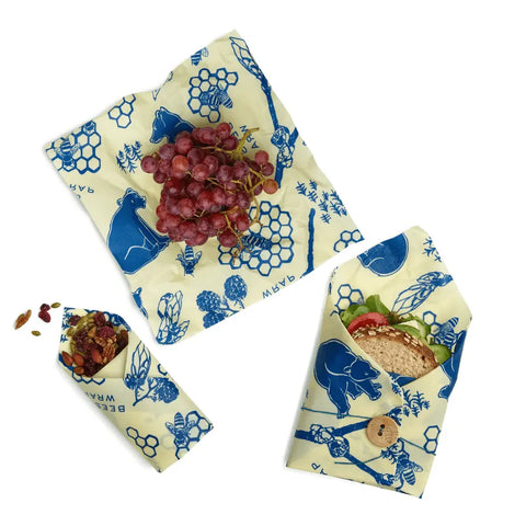 Bees Wrap The Lunch Pack features three reusable wraps with blue animal and plant designs, shown holding grapes, a sandwich, and mixed nuts or dried fruit on a white background.