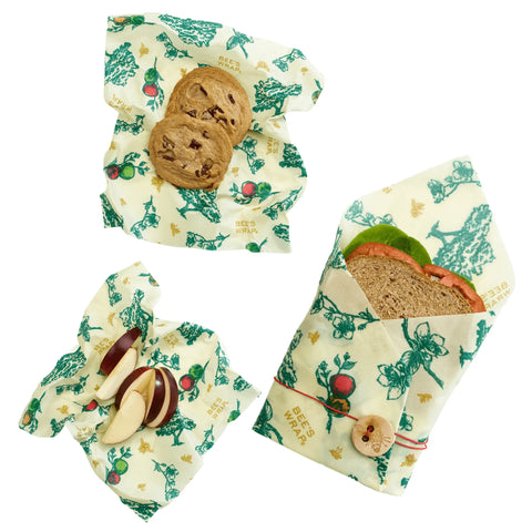 Bees Wrap The Lunch Pack includes three washable wraps in cream with green and red prints—perfect for a sandwich, sliced apples, and cookies. One wrap features a wooden button and string closure.