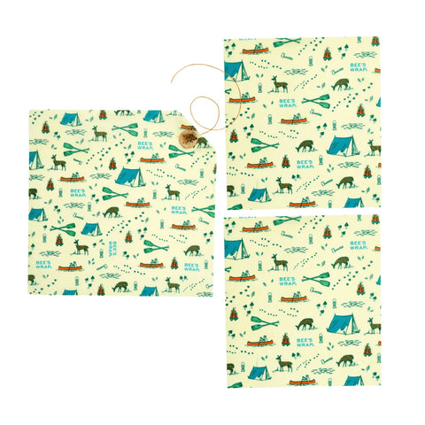 The Lunch Pack by Bees Wrap includes three washable, reusable wraps featuring camping motifs—tents, trees, campfires, animals, and canoes—in blue, green, and brown on a light background. One wrap is partially rolled with twine.