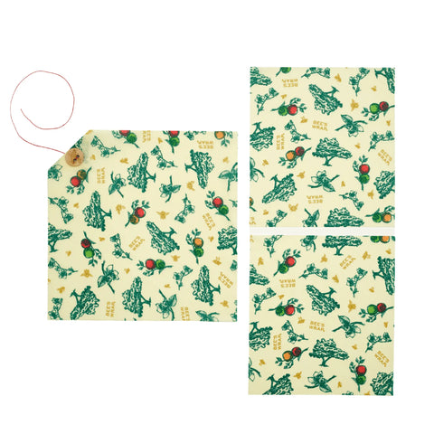 Bees Wrap The Lunch Pack includes three yellow washable wraps with green and red fruit and plant designs. One wrap features a red string and wooden button for easy securing.