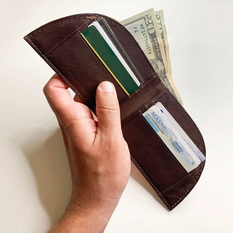 A hand holds an open Rogue Industries Rogue Front Pocket Wallet - Allagash Tan, made of top grain leather and containing credit cards, a Maine driver’s license, and twenties, all set against a plain white background.