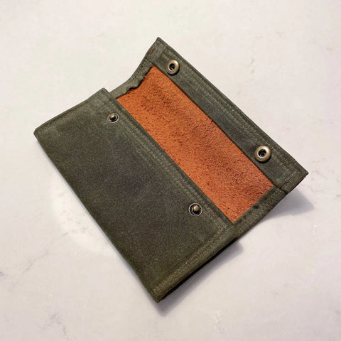 The Rogue River Fly Fishing Wallet by Rogue Industries is shown open on a light surface, displaying its brown suede interior and metal snap closures—an essential trout fishing accessory.