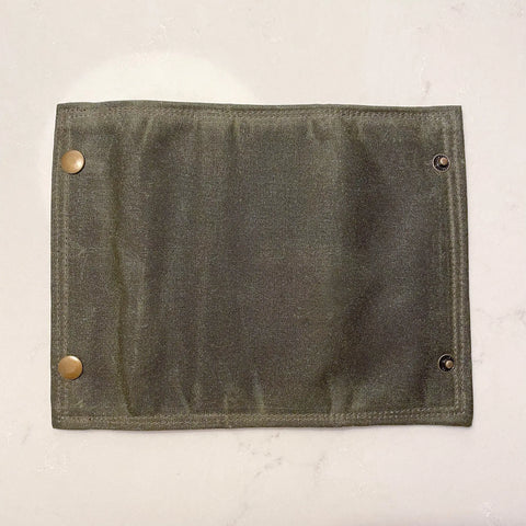 The Rogue River Fly Fishing Wallet by Rogue Industries is a rectangular dark gray waxed canvas accessory with three metal snaps per side, shown flat on a light surface—perfect for organizing your favorite trout flies.