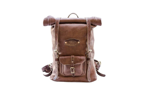 The Urban Southern Rolltop Backpack is a weather-resistant brown leather bag with two front straps and metal buckles, a small buckled front pocket, and adjustable shoulder straps, shown on a white background.
