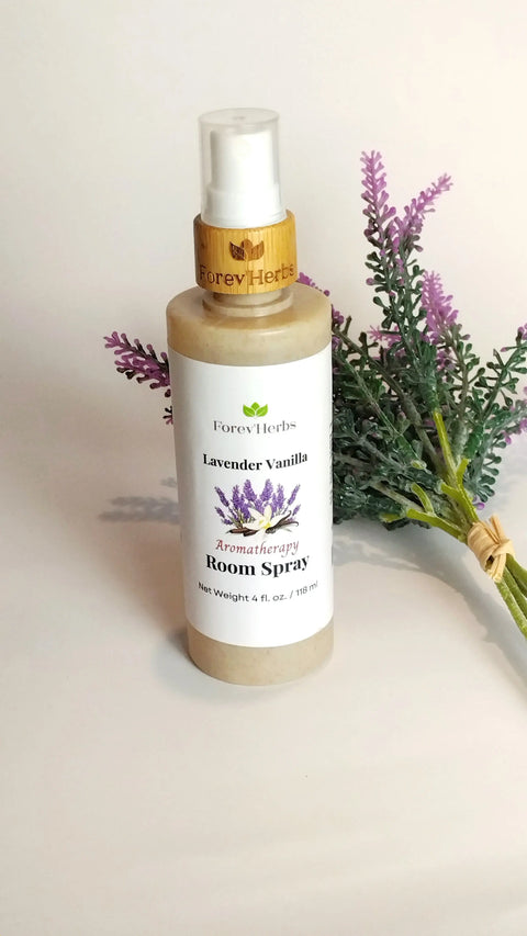 A bottle of Forev'Herbs Room Spray sits next to a small bundle of artificial lavender flowers on a white surface.