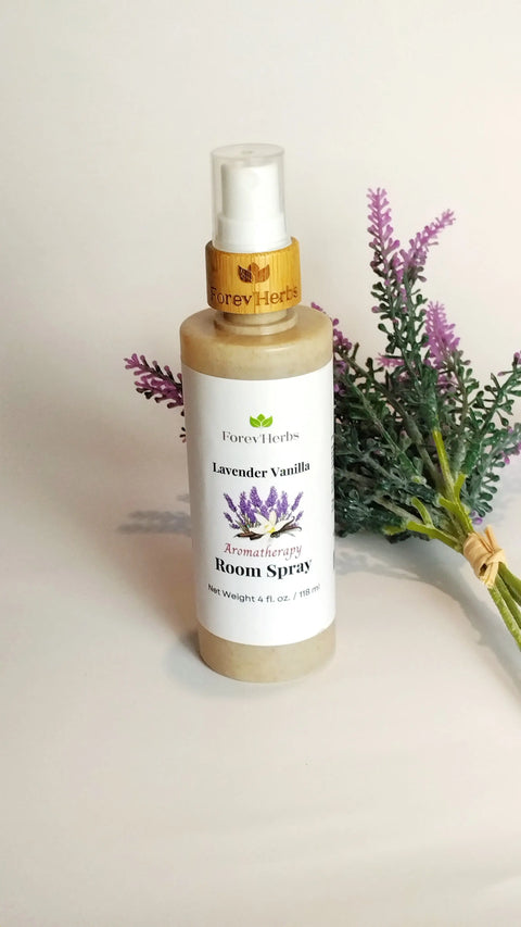A bottle of Forev'Herbs Room Spray stands upright on a white surface next to a small bouquet of artificial purple lavender flowers, offering an eco-friendly way to infuse soothing fragrance into your space.