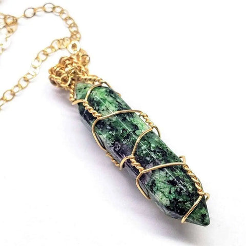 The Gold Wire Wrapped Caged in Ruby in Zoisite Pointed Crystal Necklace by Alexa Martha Designs is shown on a white background, featuring a green and black crystal pendant artistically set on a gold chain.
