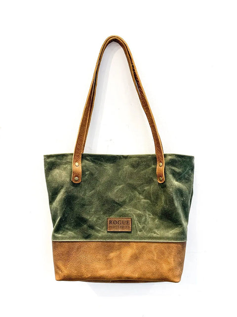 The Saco River Tote Bag by Rogue Industries features full-grain leather handles and base, an olive green waxed canvas body, and a rectangular leather patch with ROGUE INDUSTRIES on the front. The background is plain white.