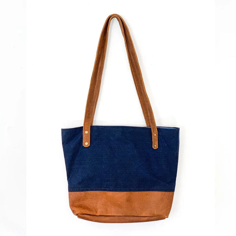 The Rogue Industries Saco River Tote Bag features a navy blue waxed canvas body with brown full-grain leather straps and bottom, crafted in Maine and shown against a plain white background.