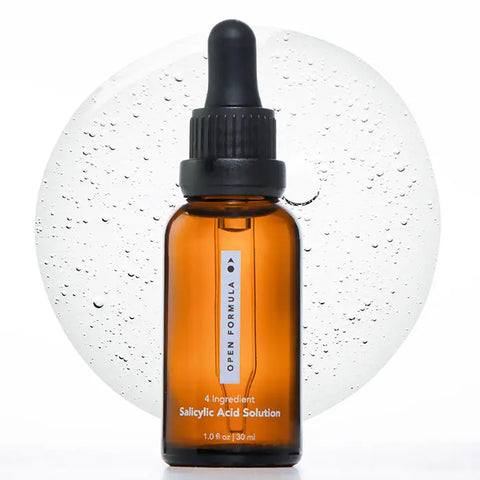 A brown glass dropper bottle labeled Open Formula Salicylic Acid Exfoliant stands before a splash of clear liquid with bubbles on a white background, highlighting its pore-unclogging and blackhead-reducing benefits.