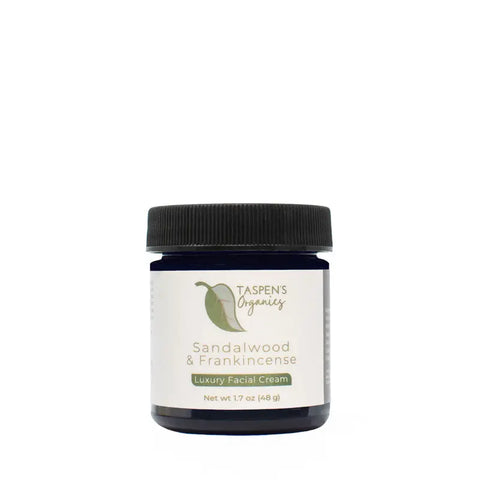 A dark blue jar with a black lid labeled Taspens Organics Sandalwood & Frankincense Luxury Facial Cream, an American-made product, net wt 1.7 oz (48 g), displayed against a white background.