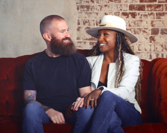 Two people sitting on a red couch in front of a brick wall.
