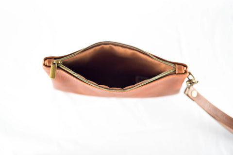 The Sebago Leather Clutch by Rogue Industries is a brown leather wristlet pouch with a zipper partially open, showing the empty interior. It features a wristlet strap and is photographed from above on a white background.