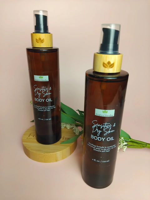 Two brown bottles of Forev'Herbs Sensitive & Dry Skin Body Oil with bamboo caps are displayed on a wooden stand, complemented by green leaves and small white flowers against a soft peach backdrop.