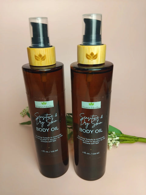 Two brown pump bottles labeled Forev'Herbs Sensitive & Dry Skin Body Oil stand side by side on a light surface, with small white flowers and green leaves in the background.