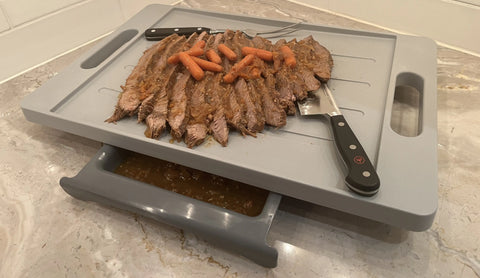 Sliced roast beef with carrots rests on the Karving King Set of 2 Dripless Cutting Boards 2 in 1 System; juices flow to a pull-out tray beneath the board, all set on a marble countertop.