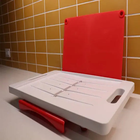 The Karving King Set of 2 Dripless Cutting Boards 2 in 1 System, featuring grooves, handles, and an upright red section for dripless carving, sits on a countertop against a yellow tiled backsplash.