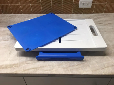 A Karving King Set of 2 Dripless Cutting Boards 2 in 1 System—a white rectangular board with handle and a blue flexible mat—rests on a marble countertop, with the blue grip piece beneath to hold it securely in place.