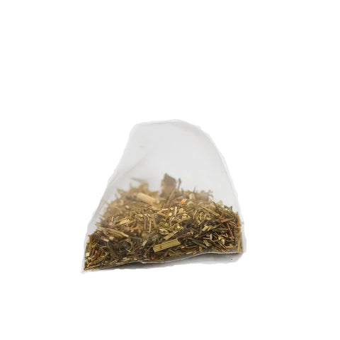 A close-up of a transparent, pyramid-shaped tea bag of Sasquatch Tea Cos Shenandoah Sunset (Green Rooibos Herbal Tea), showing greenish-brown caffeine-free leaves and stems inside, set against a white background.