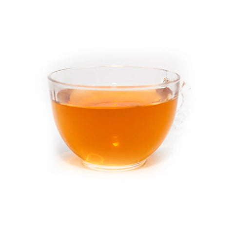 A clear glass cup filled with amber-colored Shenandoah Sunset Green Rooibos Herbal Tea by Sasquatch Tea Co, set on a plain white background.