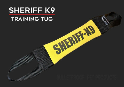 A yellow and black Sheriff K9 Fire Hose Training Tug by Bulletproof Pet Products Inc, featuring handles at both ends and “SHERIFF-K9” labeling, is shown on a dark background with bold “SHERIFF K9 TRAINING TUG” text.