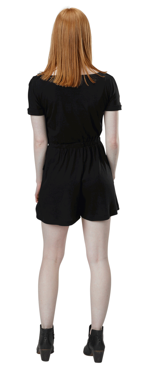 A person with straight, shoulder-length red hair stands facing away from the camera, wearing a black Spiritex Short Sleeve Surplice Romper made of Organic Cotton/Tencel and black ankle boots.