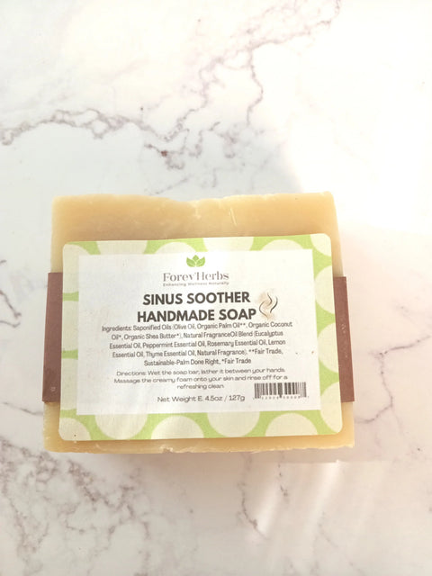 A bar of Sinus Soother Handmade Soap by Forev'Herbs rests on a white surface. Made with olive oil, coconut oil, shea butter, peppermint, and eucalyptus essential oils, it helps relieve congestion naturally.