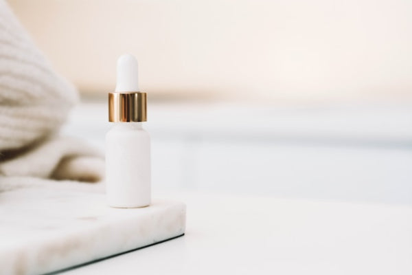 White skincare dropper bottle with gold cap on a light surface