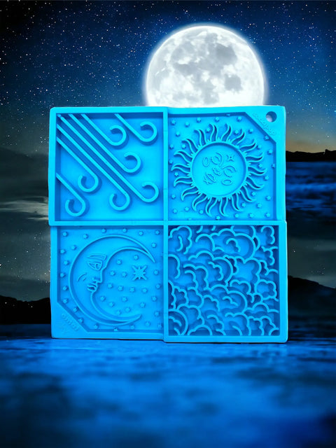 The SodaPup Sky Design EMat Enrichment Lick Mat, featuring wind, sun, moon, and cloud sections in blue silicone, stands upright against a glowing full moon and starry sky—creating a calming scene to support dog digestive health.