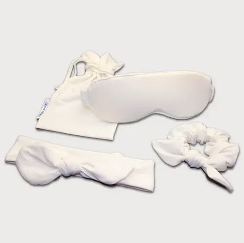The Goodnighties Accessories Value Pack features white sleepwear essentials—a sleep mask, drawstring pouch, scrunchie, and bow headband—beautifully arranged on a plain light background.