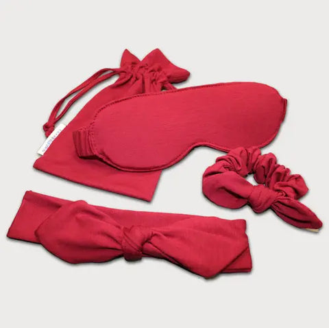 The Goodnighties Accessories Value Pack includes red fabric essentials: an American-made sleep mask, drawstring pouch, knotted headband, and scrunchie—all neatly displayed against a neutral backdrop.