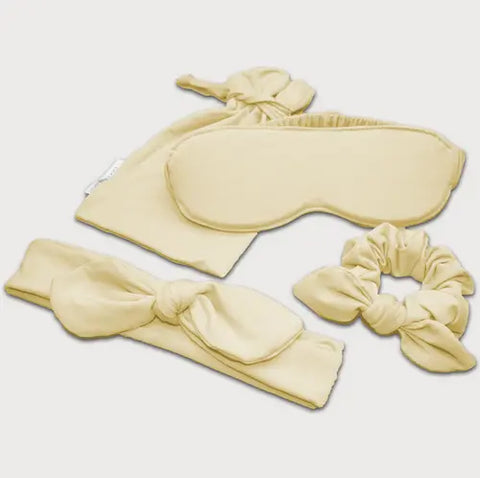 The Goodnighties Accessories Value Pack includes pale yellow sleepwear essentials—a sleep mask, fabric pouch, knotted headband, and scrunchie—all arranged on a white background.