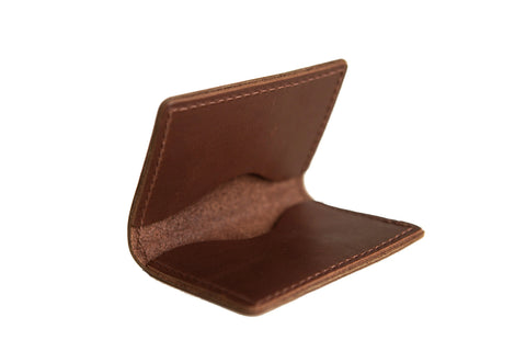 The Urban Southern Bifold Card Wallet, crafted from brown full-grain leather with visible edge stitching, is shown open and empty on a white background, emphasizing its simple design.