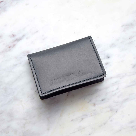 The Urban Southern Bifold Card Wallet, crafted from full-grain leather, is closed and displayed on a white marble surface with subtle gray and pink veins.