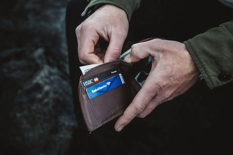 A person in a green jacket holds an open Rogue Industries Football Leather Front Pocket Wallet, showing cash and two visible credit cards—one from HSBC and one from Bank of America.