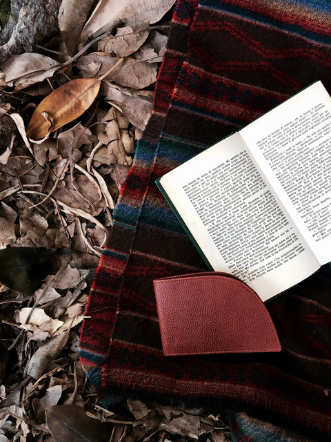 An open book and a Rogue Industries Football Leather Front Pocket Wallet rest on a striped blanket, which lies atop dry autumn leaves scattered across the ground.