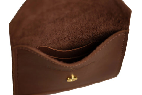 A close-up view of the Urban Southern Postal Crossbody, highlighting its brown leather, minimalist design, inner pocket, and gold-colored snap button on the front.
